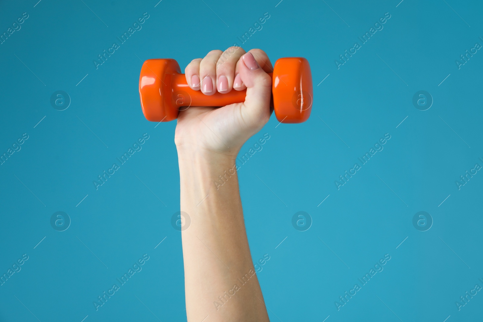 Photo of Woman exercising with dumbbell on light blue background, closeup