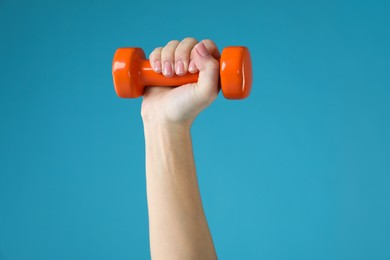 Photo of Woman exercising with dumbbell on light blue background, closeup