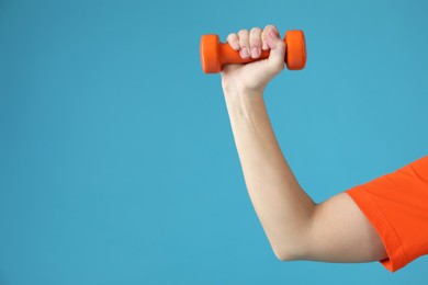 Photo of Woman exercising with dumbbell on light blue background, closeup. Space for text