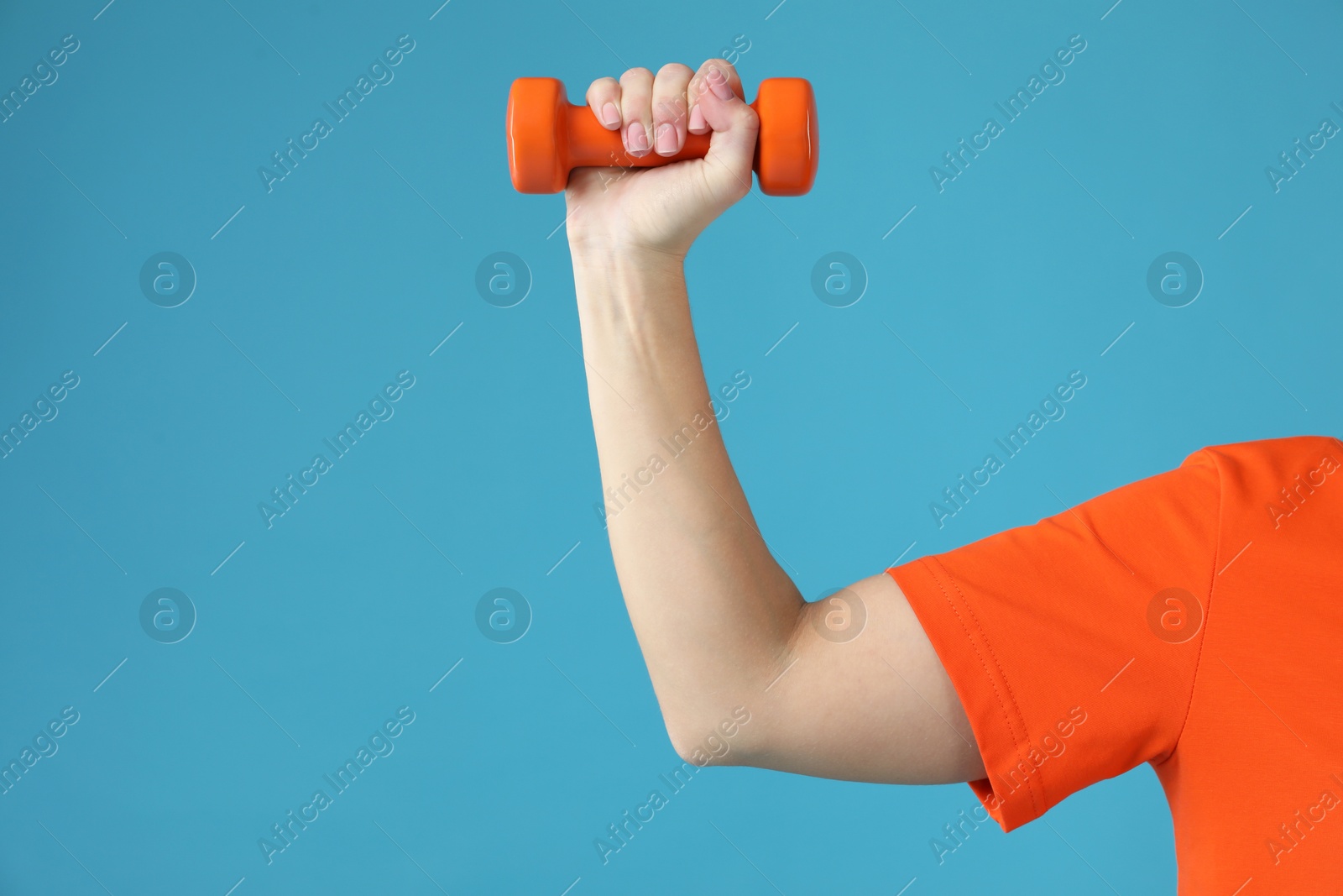 Photo of Woman exercising with dumbbell on light blue background, closeup