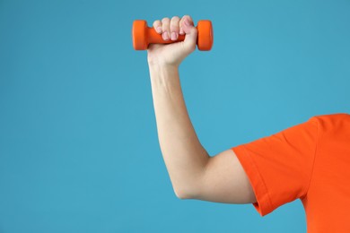 Woman exercising with dumbbell on light blue background, closeup