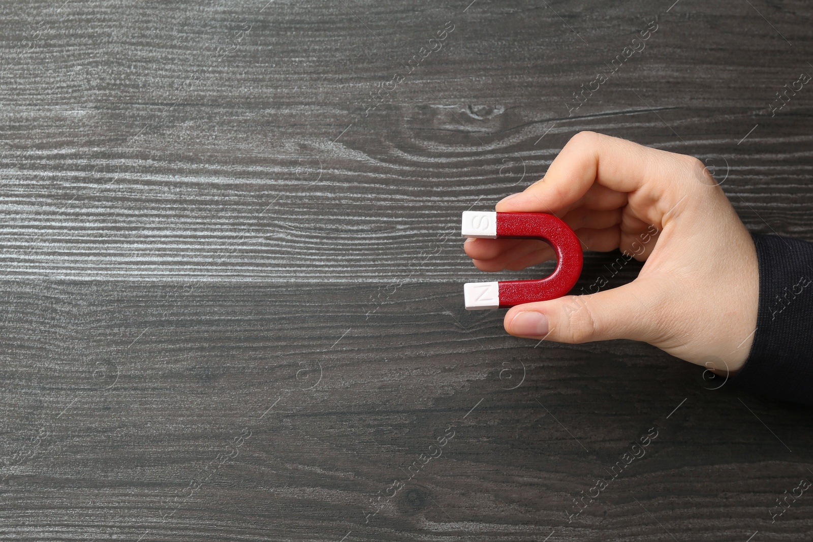 Photo of Woman with horseshoe magnet on wooden background, top view. Space for text