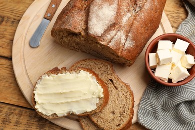 Photo of Fresh bread with butter and knife on wooden table, flat lay