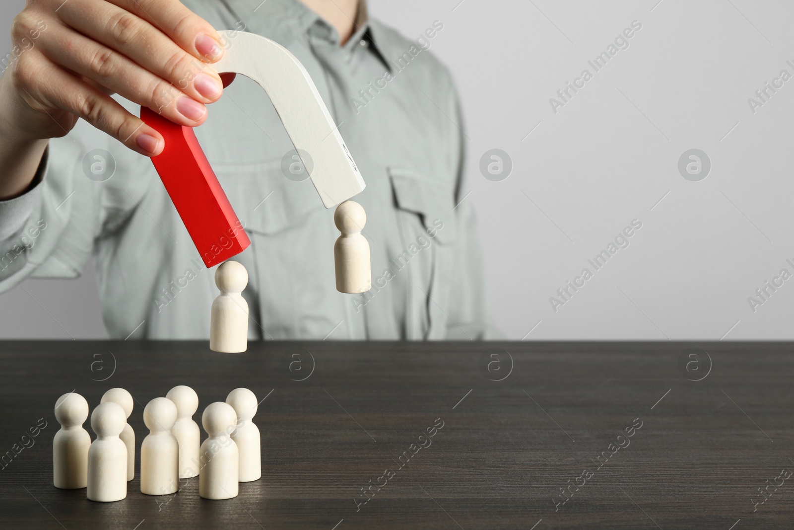 Photo of Woman with magnet attracting human figures at wooden table, closeup. Space for text