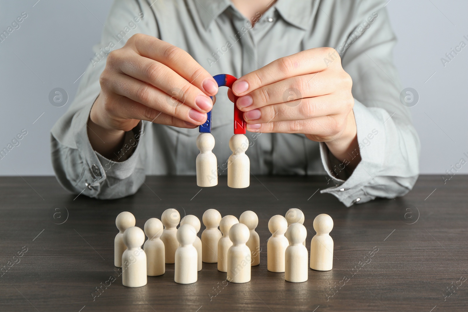 Photo of Woman with magnet attracting human figures at wooden table, closeup