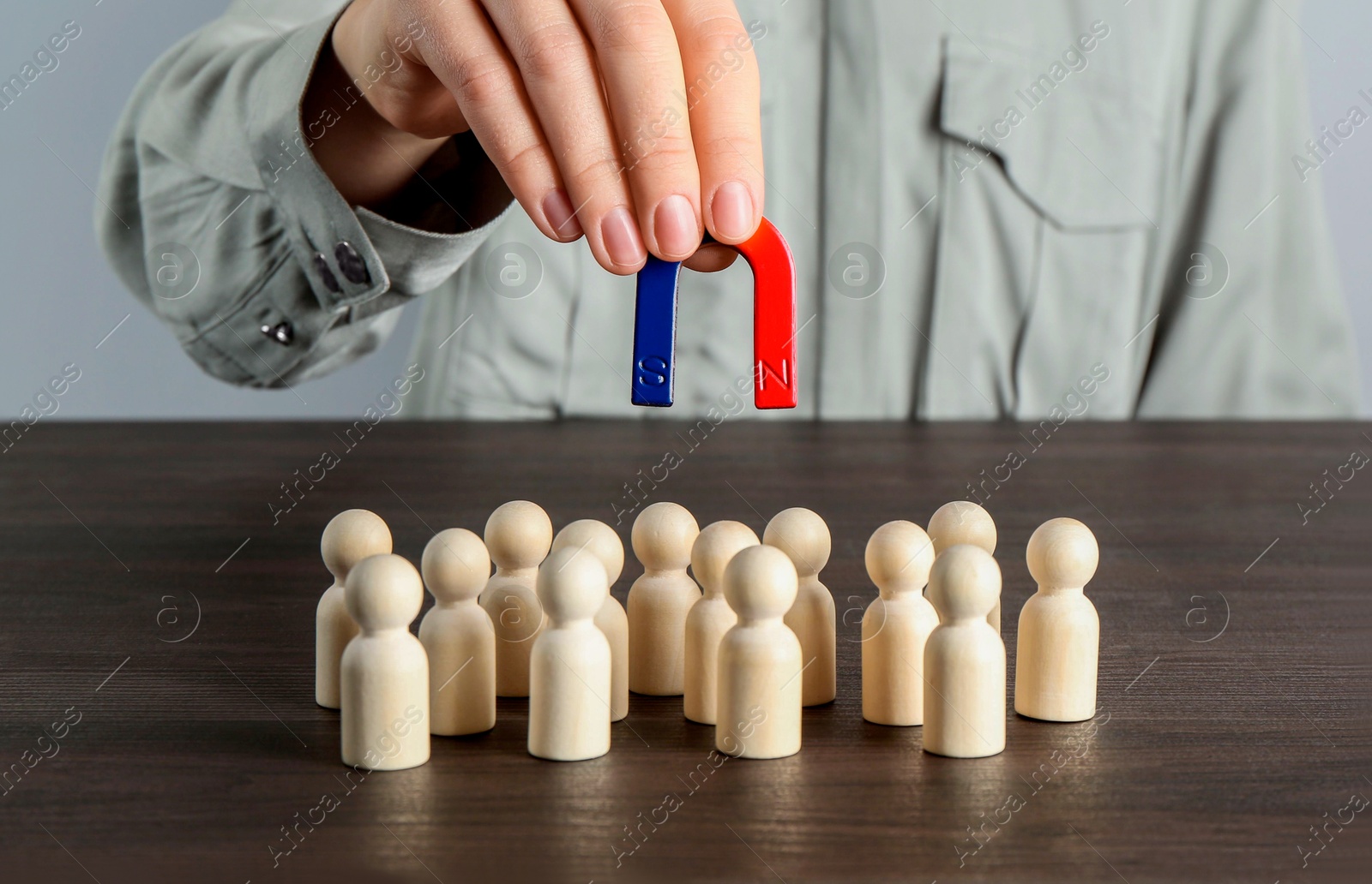 Photo of Woman with magnet attracting human figures at wooden table, closeup