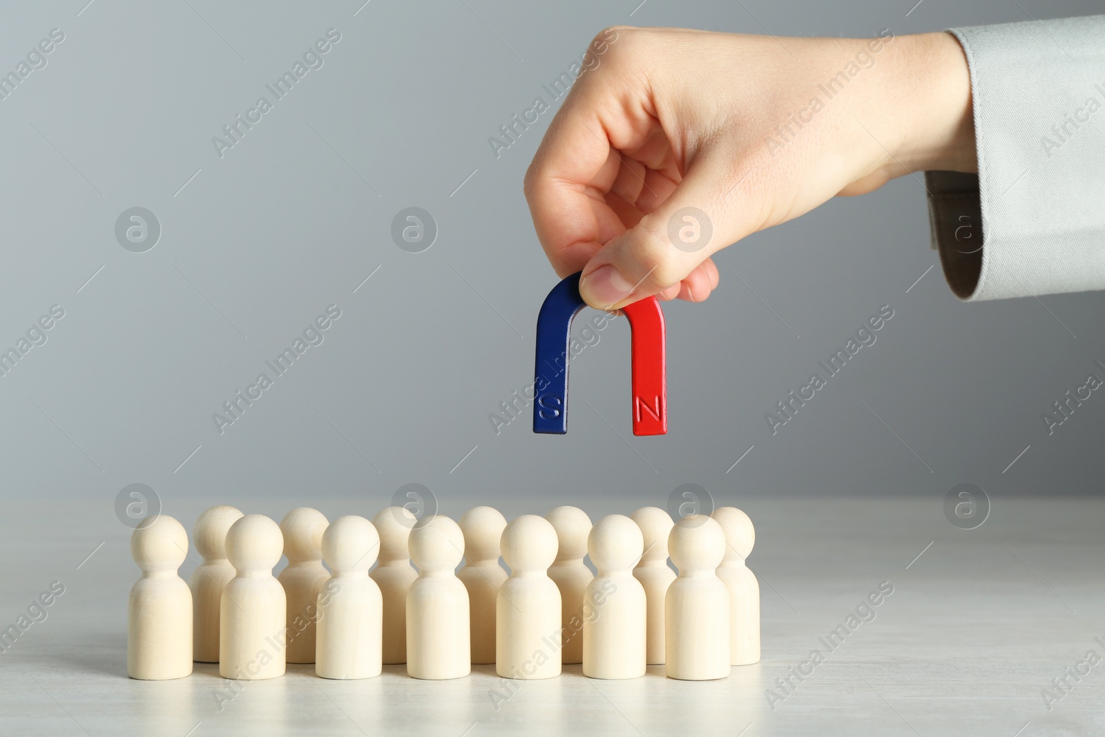 Photo of Woman with magnet attracting wooden human figures at light table, closeup