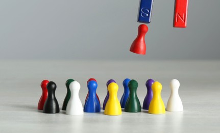 Photo of Attracting red game piece among other ones with magnet at light table, closeup