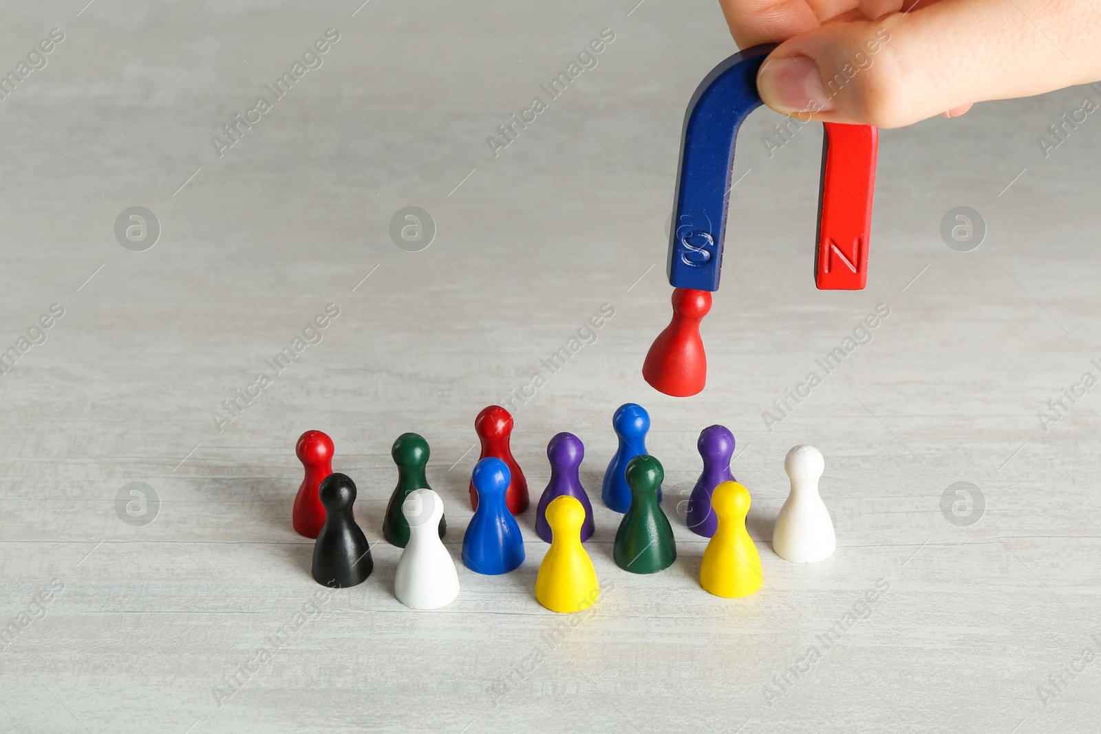 Photo of Woman with magnet attracting red game piece among other ones at light table, closeup