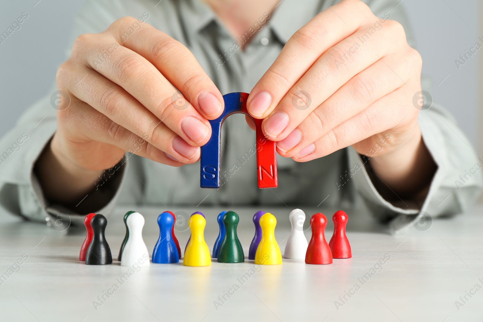 Photo of Woman with magnet attracting colorful game pieces at light table, closeup