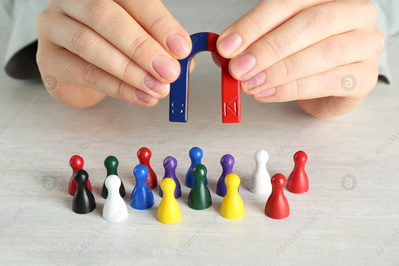 Photo of Woman with magnet attracting colorful game pieces at light table, closeup