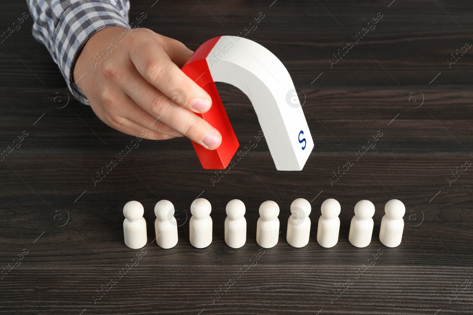 Photo of Man with magnet attracting human figures at wooden table, closeup