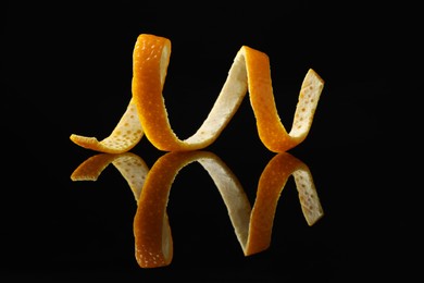 Photo of One fresh orange peel on black mirror surface