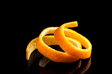 Photo of One fresh orange peel on black mirror surface, closeup