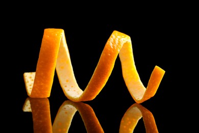 Photo of One fresh orange peel on black mirror surface, closeup