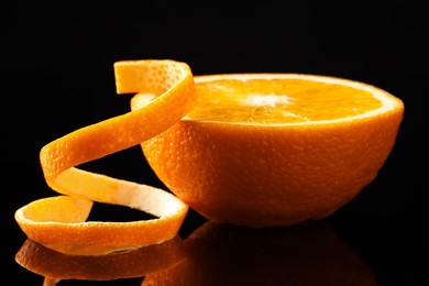 Photo of Fresh orange peel and half of fruit on black mirror surface, closeup