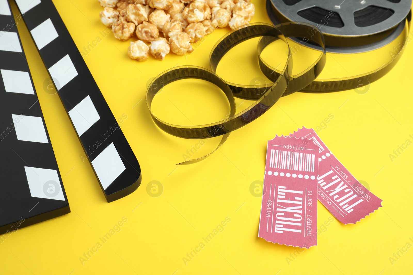 Photo of Movie clapper, sweet popcorn, tickets and film reel on yellow background, closeup