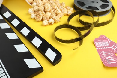 Photo of Movie clapper, sweet popcorn, tickets and film reel on yellow background, closeup