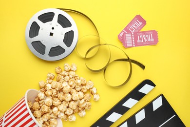 Photo of Movie clapper, sweet popcorn, tickets and film reel on yellow background, flat lay