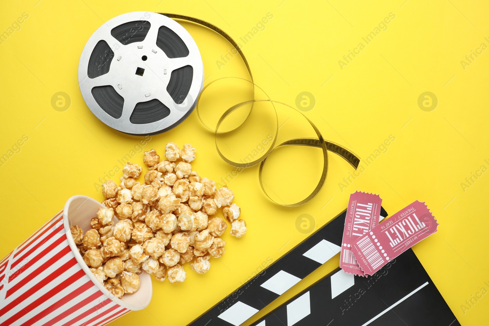 Photo of Movie clapper, sweet popcorn, tickets and film reel on yellow background, flat lay