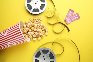 Movie tickets, sweet popcorn and film reels on yellow background, flat lay