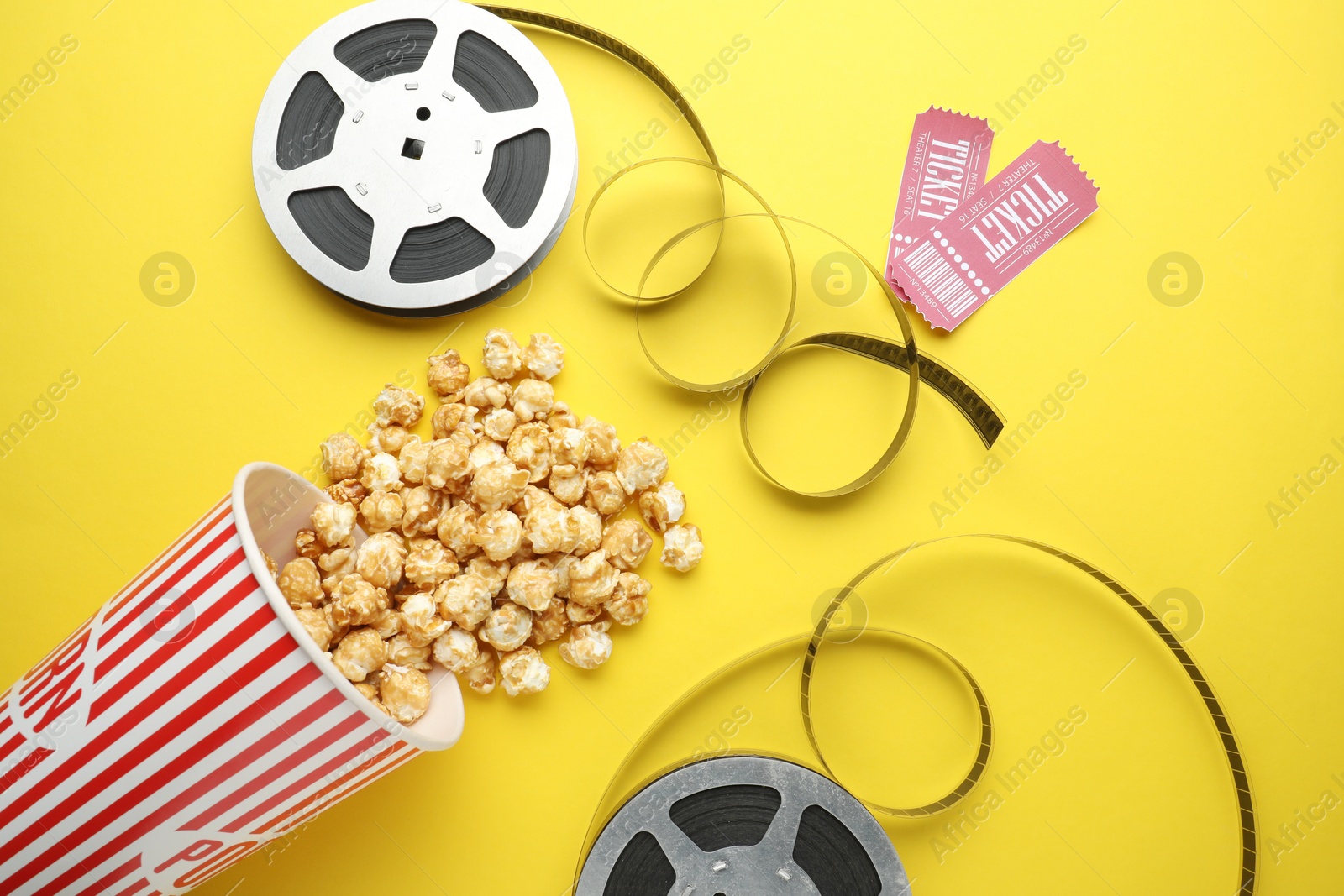 Photo of Movie tickets, sweet popcorn and film reels on yellow background, flat lay