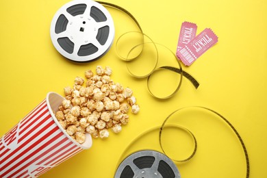 Movie tickets, sweet popcorn and film reels on yellow background, flat lay