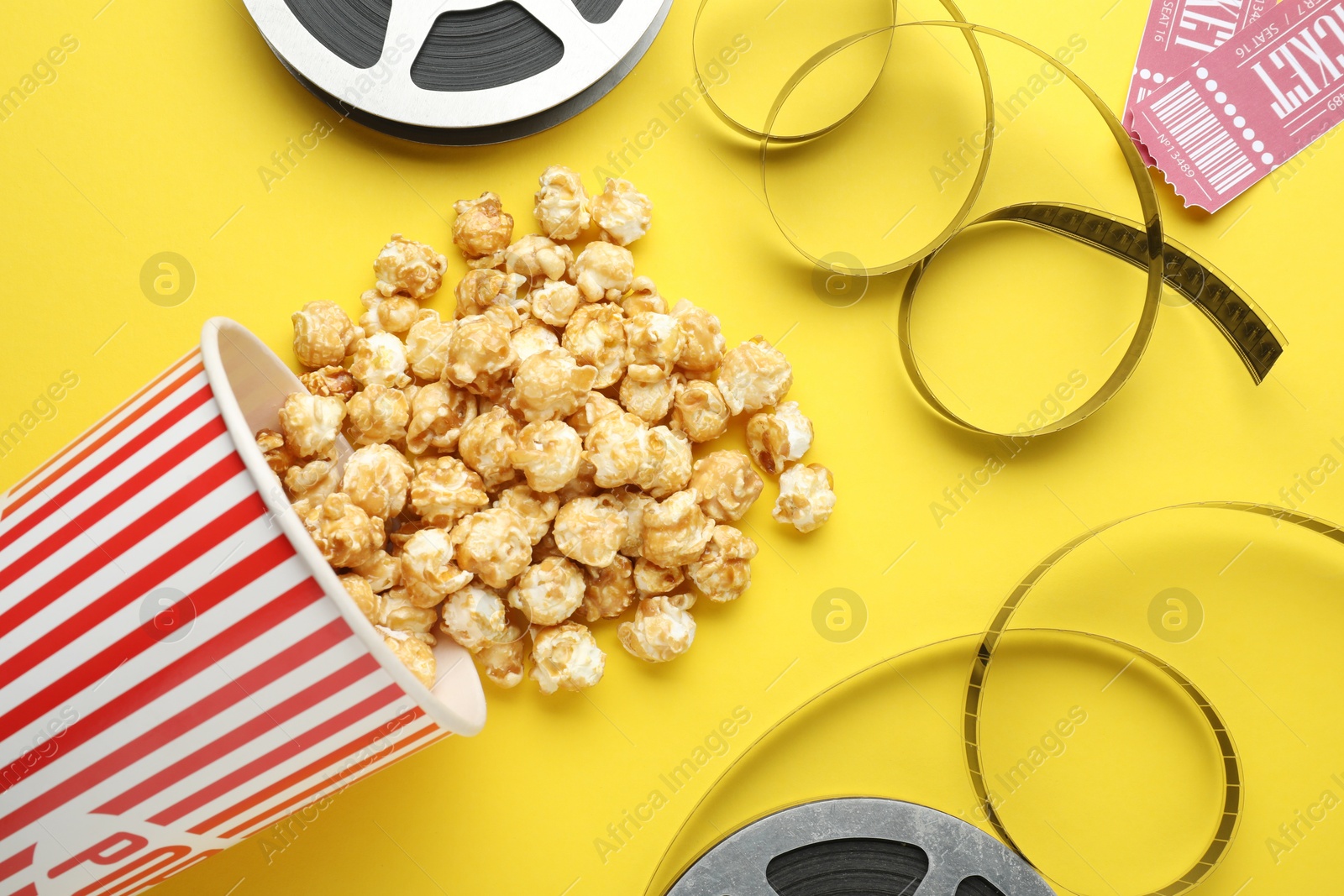 Photo of Movie tickets, sweet popcorn and film reels on yellow background, flat lay