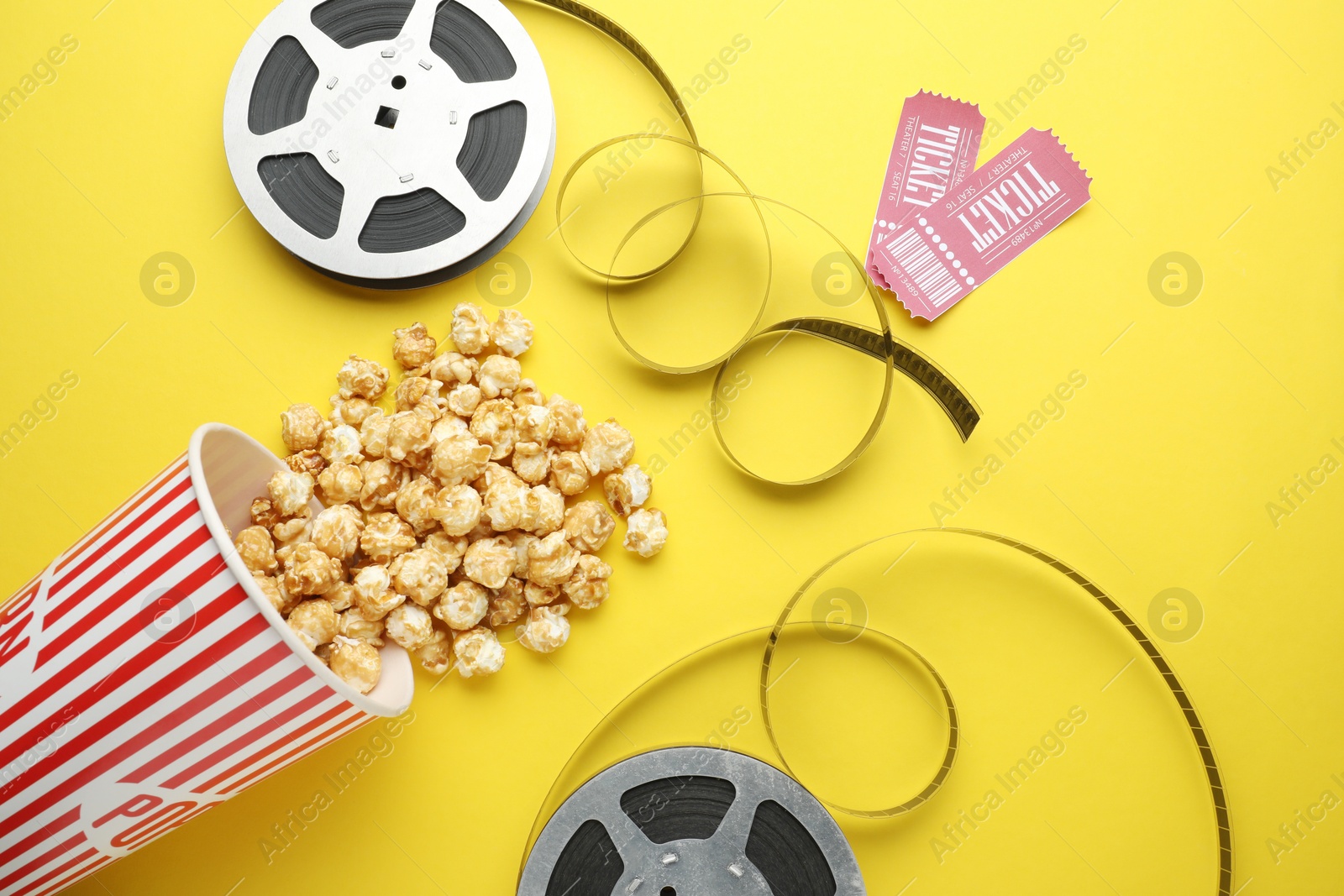 Photo of Movie tickets, sweet popcorn and film reels on yellow background, flat lay