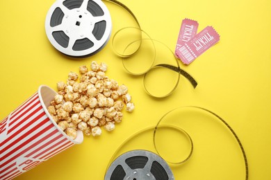 Movie tickets, sweet popcorn and film reels on yellow background, flat lay