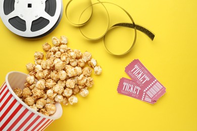 Photo of Movie tickets, sweet popcorn and film reel on yellow background, flat lay