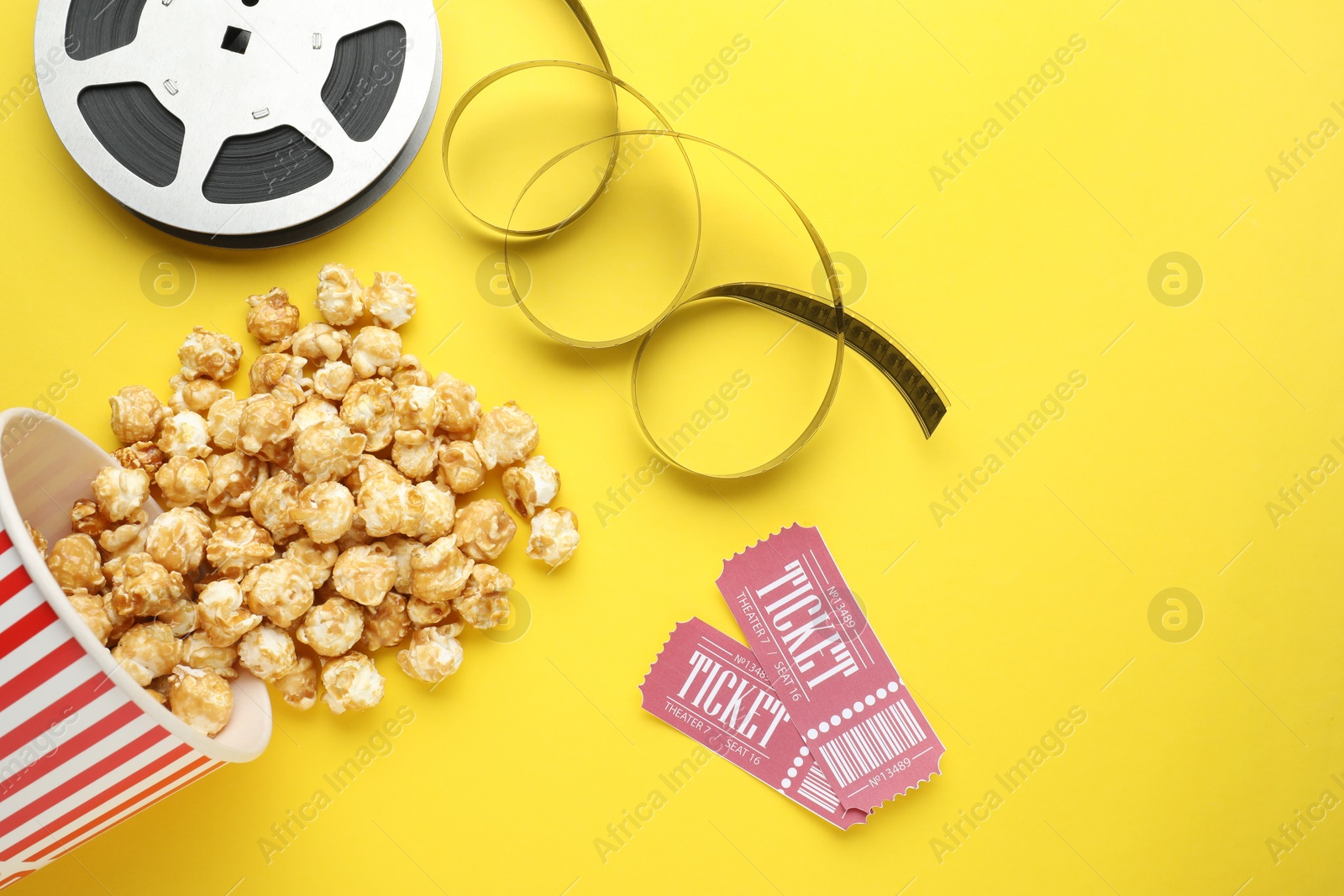 Photo of Movie tickets, sweet popcorn and film reel on yellow background, flat lay