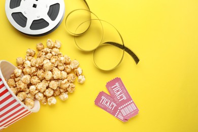 Photo of Movie tickets, sweet popcorn and film reel on yellow background, flat lay