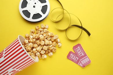 Photo of Movie tickets, sweet popcorn and film reel on yellow background, flat lay