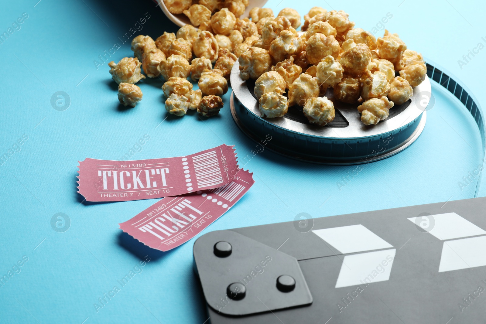 Photo of Movie clapper, sweet popcorn, tickets and film reel on light blue background, closeup