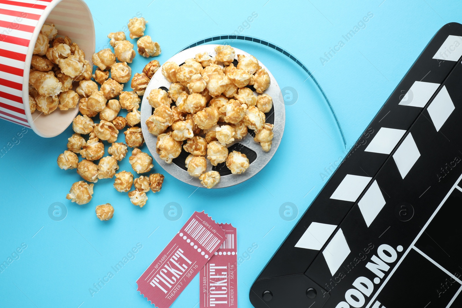 Photo of Movie clapper, sweet popcorn, tickets and film reel on light blue background, flat lay