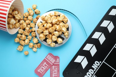 Photo of Movie clapper, sweet popcorn, tickets and film reel on light blue background, flat lay