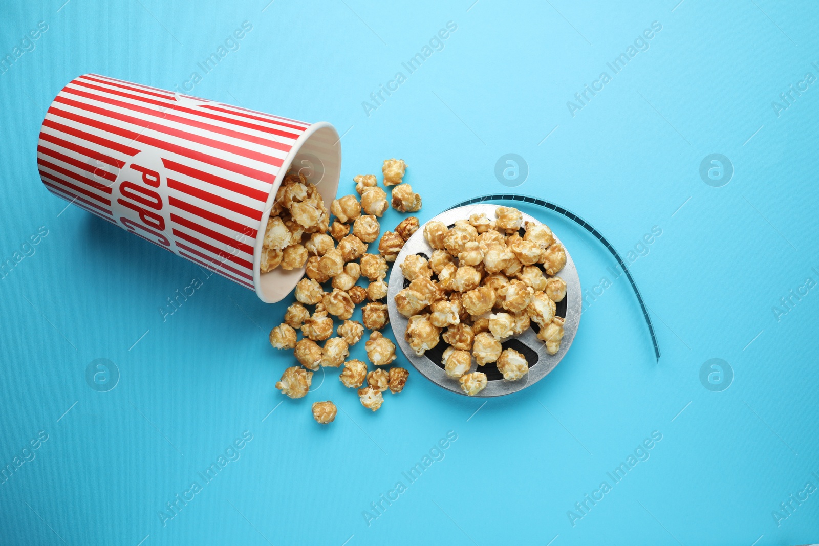 Photo of Sweet popcorn and film reel on light blue background, top view. Watching movie