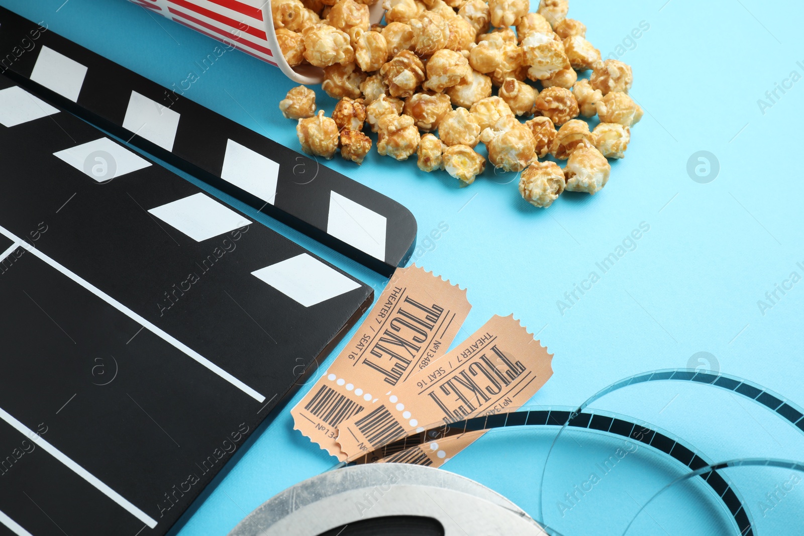 Photo of Movie clapper, sweet popcorn, tickets and film reel on light blue background, closeup