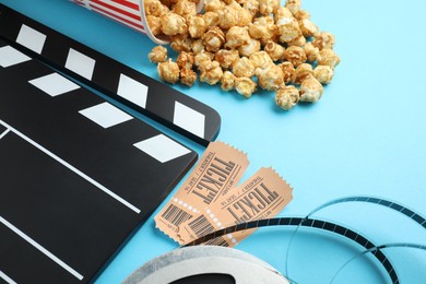 Photo of Movie clapper, sweet popcorn, tickets and film reel on light blue background, closeup