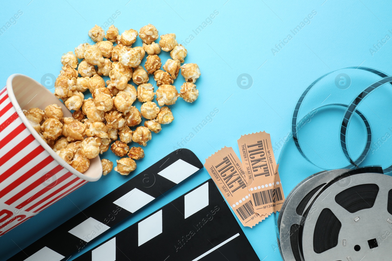 Photo of Movie clapper, sweet popcorn, tickets and film reel on light blue background, flat lay