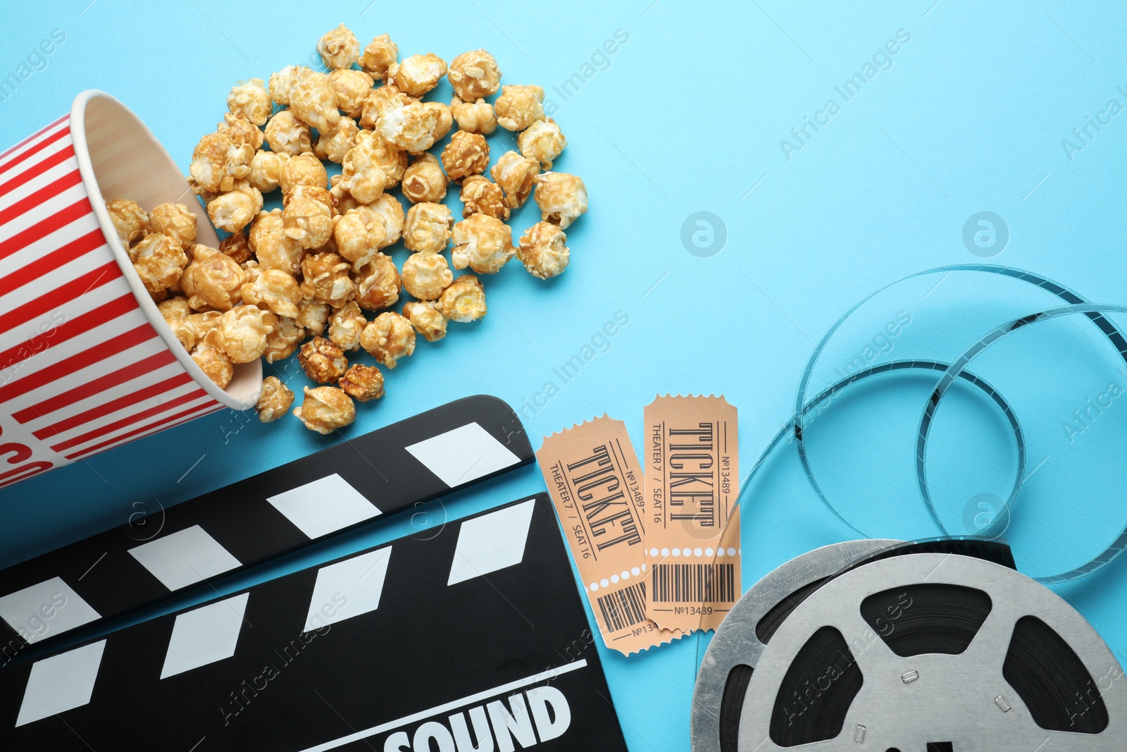 Photo of Movie clapper, sweet popcorn, tickets and film reel on light blue background, flat lay