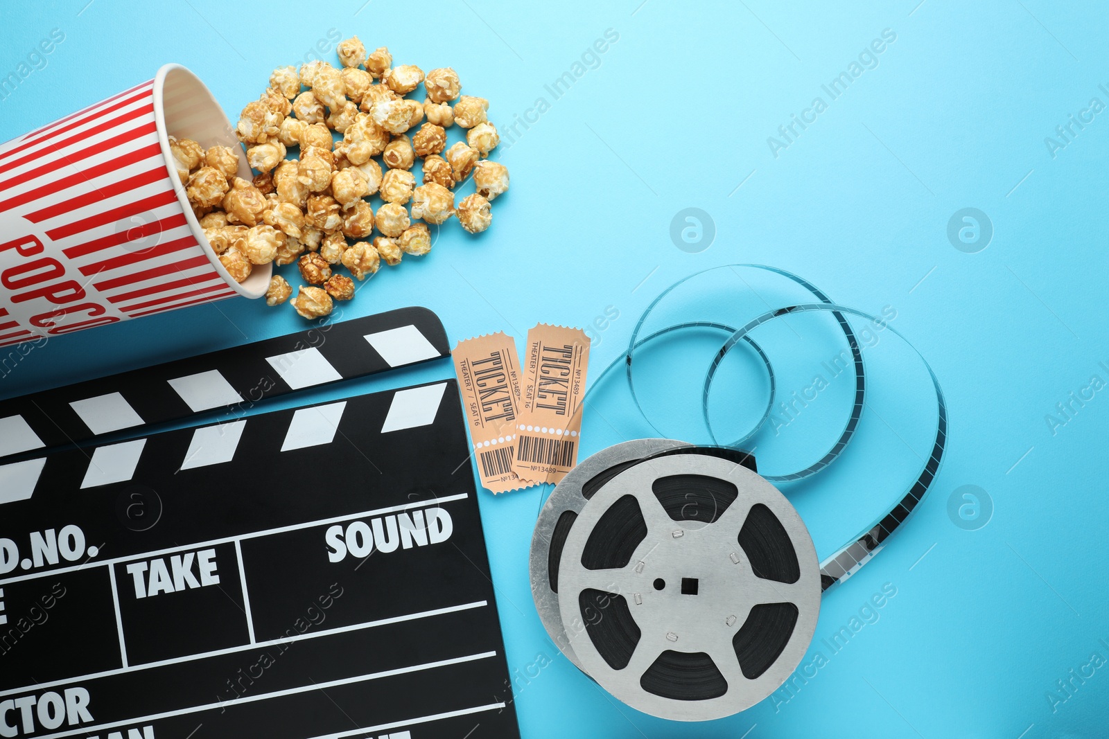 Photo of Movie clapper, sweet popcorn, tickets and film reel on light blue background, flat lay