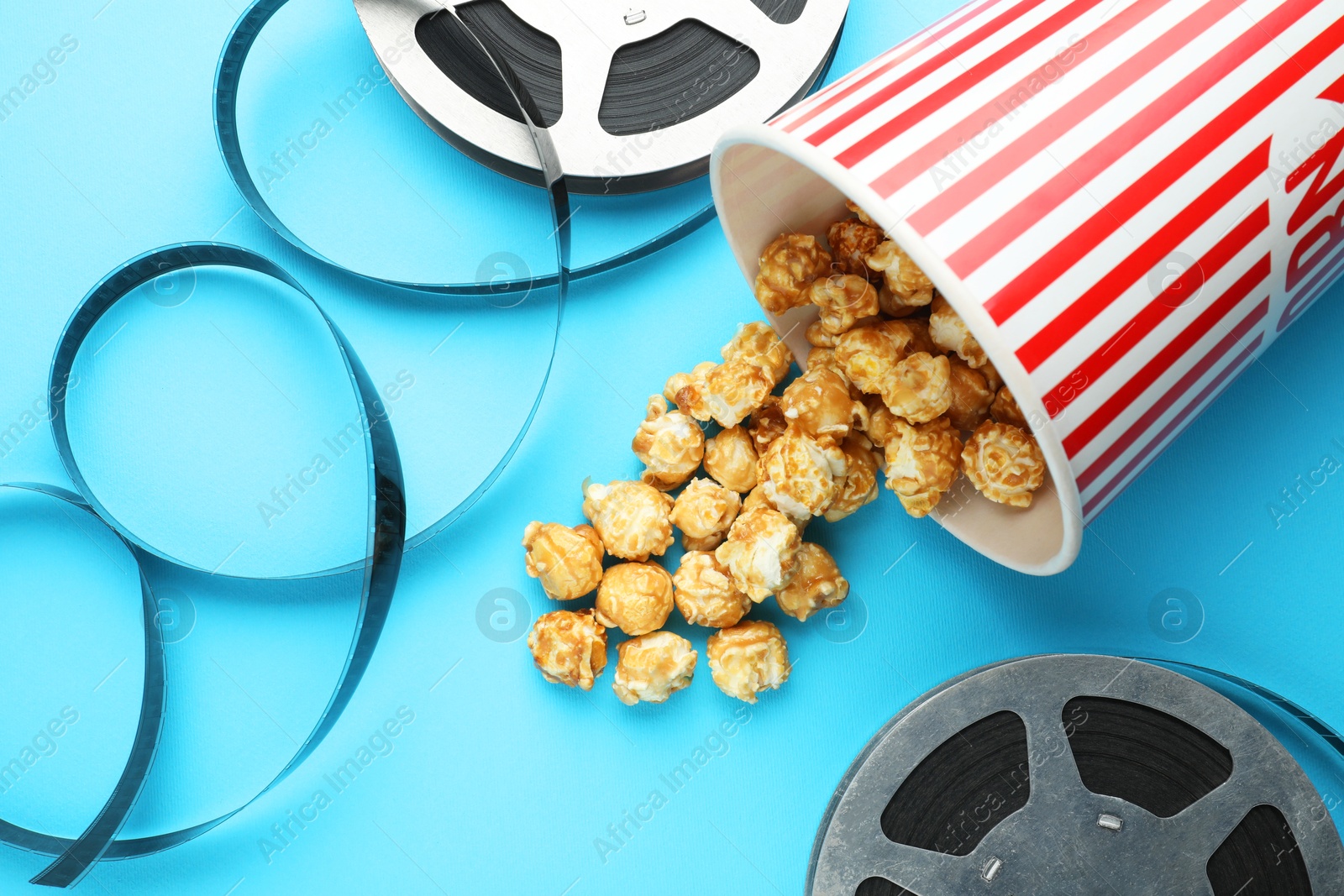 Photo of Sweet popcorn and film reels on light blue background, flat lay