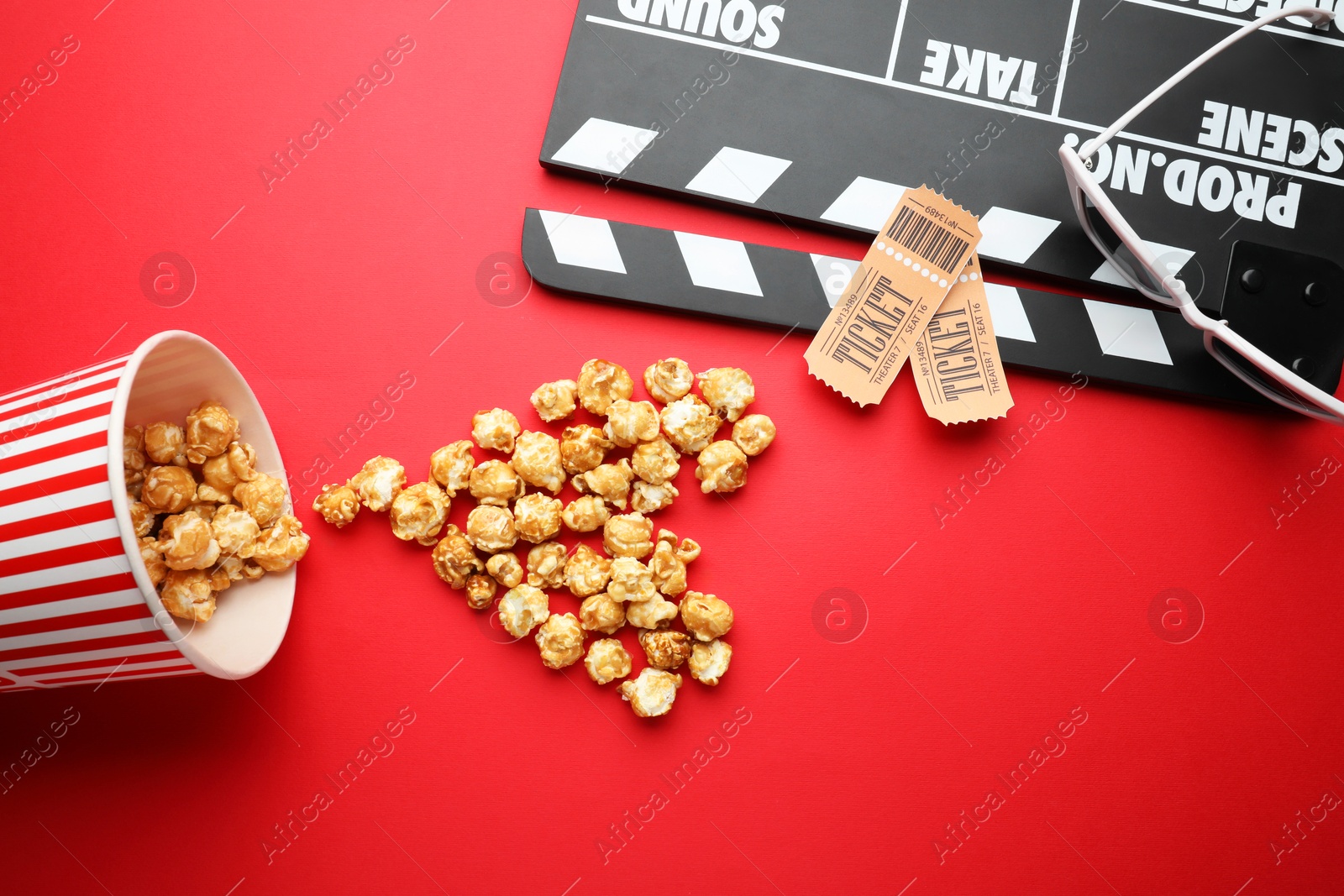 Photo of Movie clapper, sweet popcorn and tickets on red background, flat lay