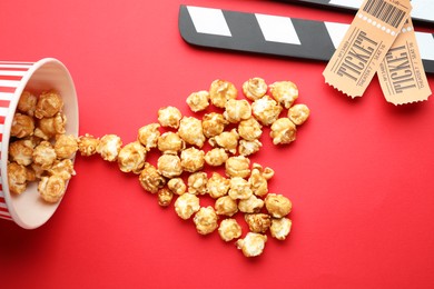 Photo of Movie clapper, sweet popcorn and tickets on red background, flat lay