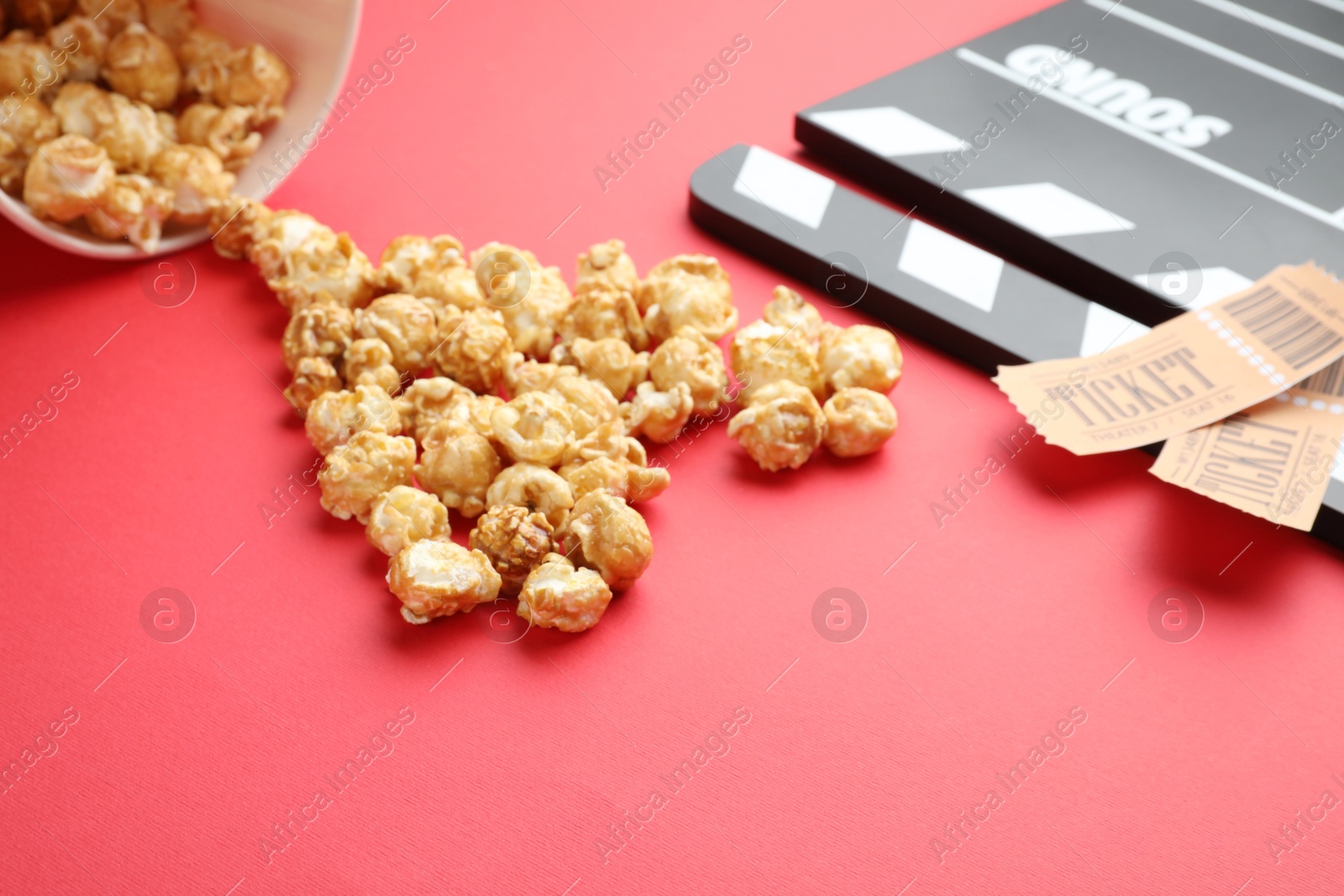 Photo of Movie clapper, sweet popcorn and tickets on red background, closeup