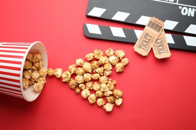 Photo of Movie clapper, sweet popcorn and tickets on red background, flat lay