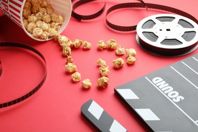 Photo of Movie clapper, sweet popcorn and film reel on red background, closeup