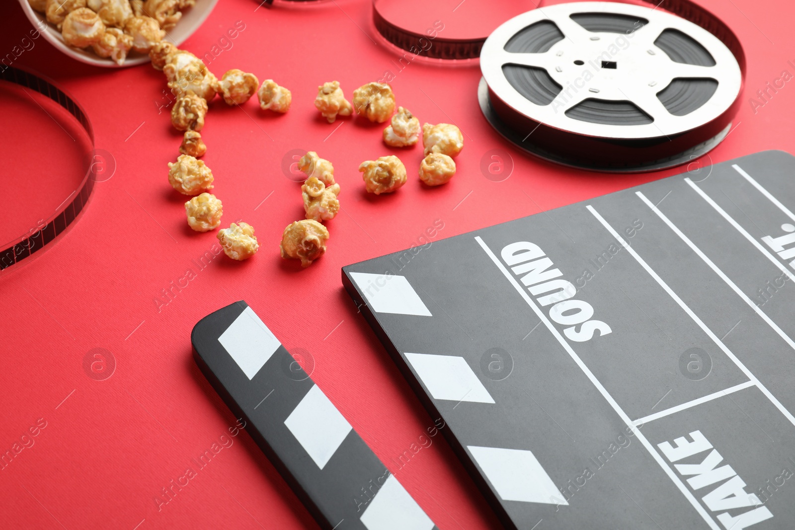 Photo of Movie clapper, sweet popcorn and film reel on red background, closeup